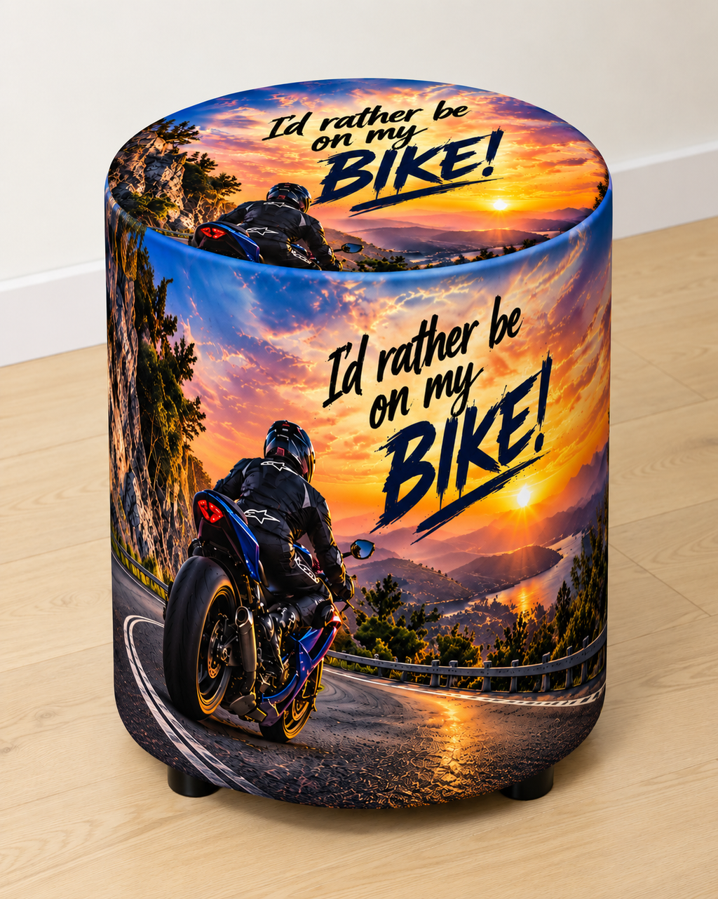 I’d Rather Be on My Bike round printed ottoman featuring a motorcycle, open-road scenery and bold orange and blue artwork
